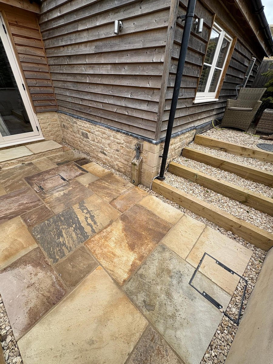After: an Indian sandstone patio with sleeper steps rising beside the building