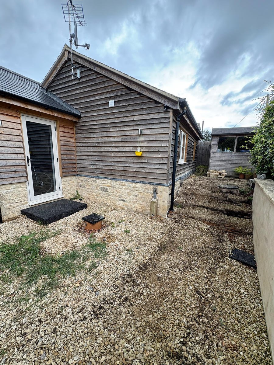 Before: rough gravel and bare ground alongside a timber-clad building