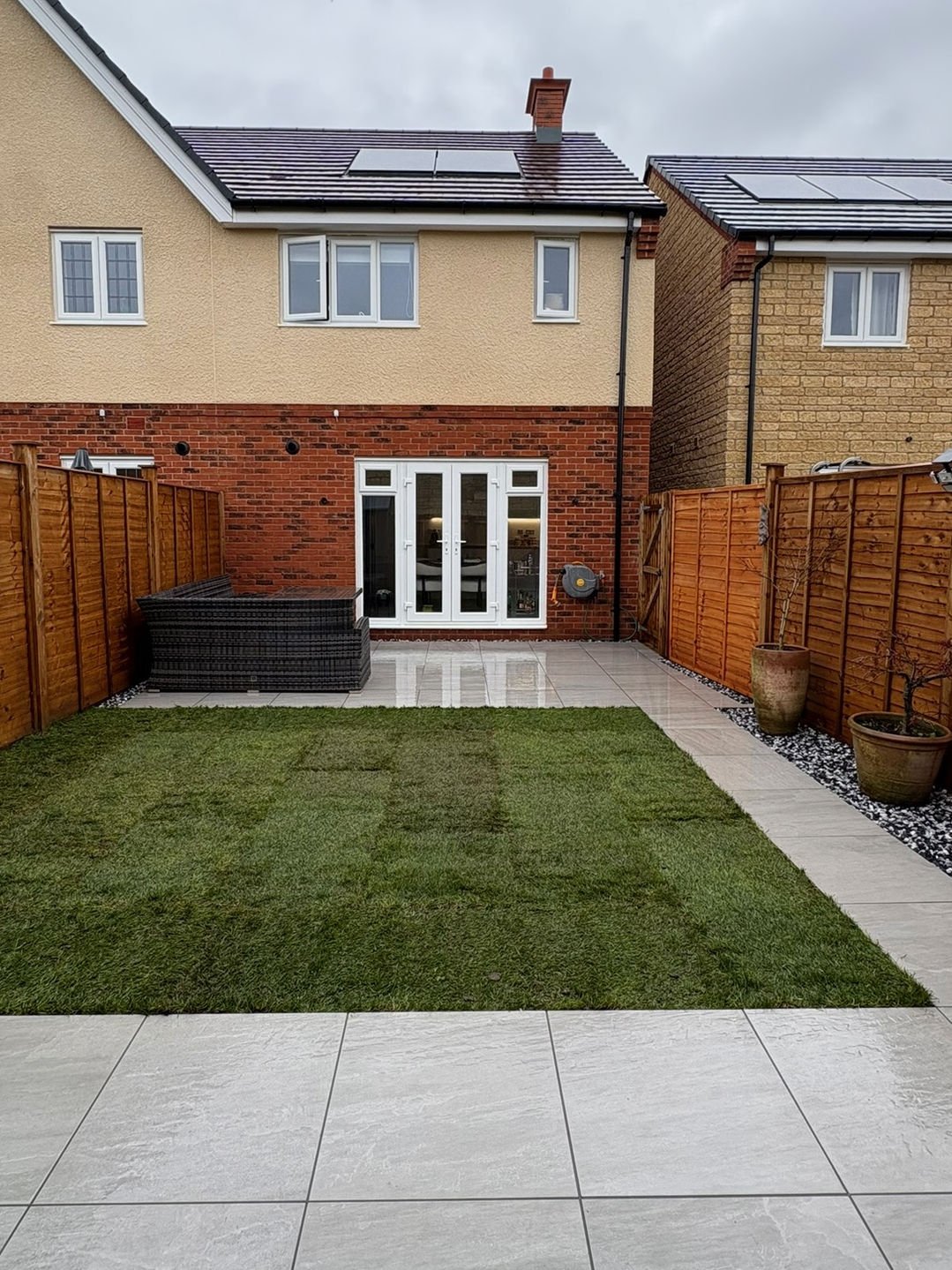 After: a porcelain terrace off the back doors with fresh turf and a shingle margin