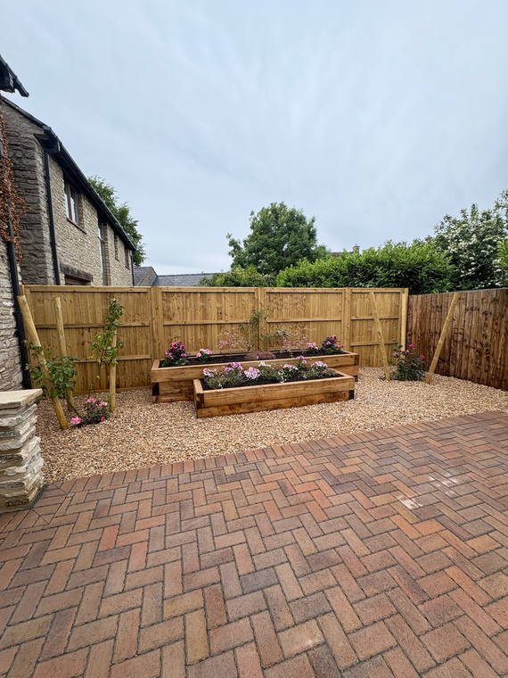 Block paving with sleeper-built raised beds planted up along a fence line