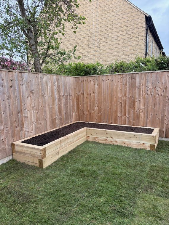 An L-shaped sleeper raised bed built into the corner of a lawn