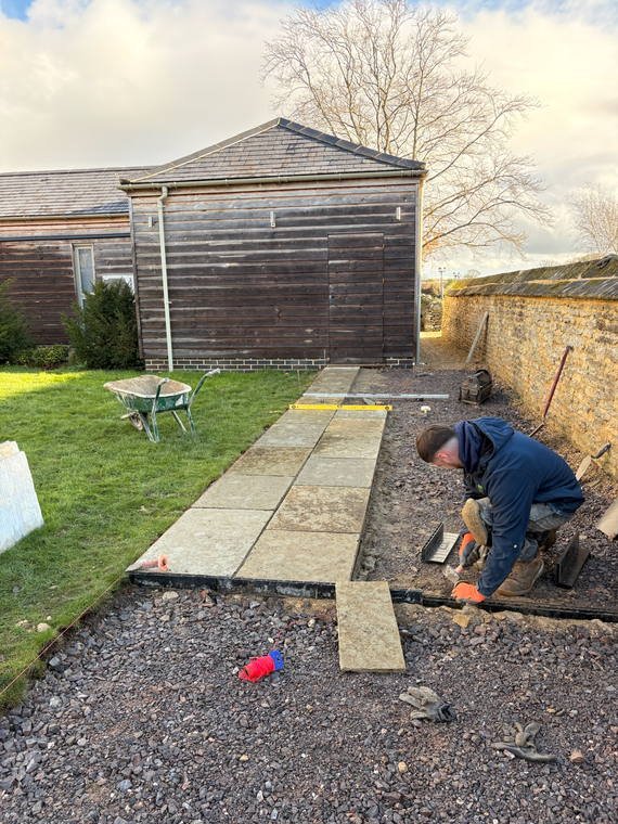 Sandstone paving being laid a course at a time outside a stone barn