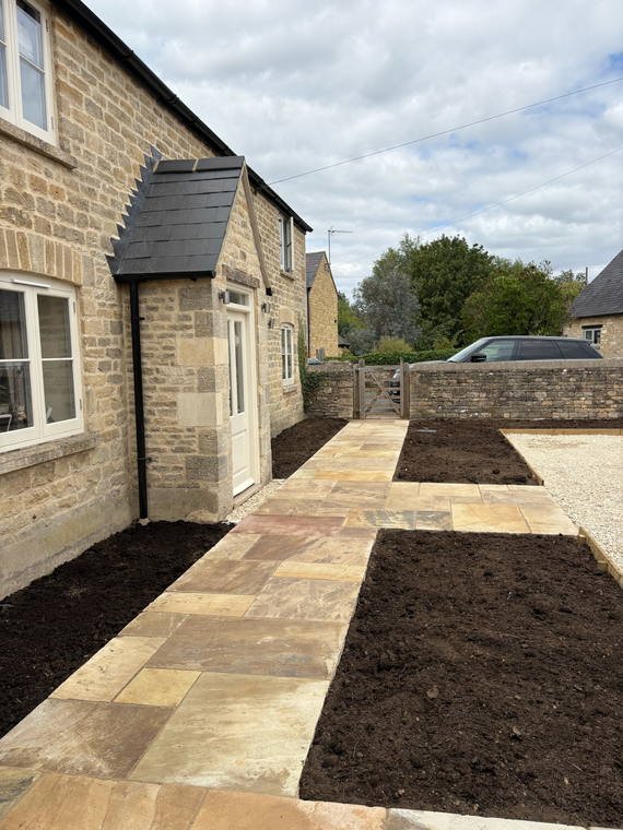 Sandstone paving and new planting beds across the front of a Cotswold cottage