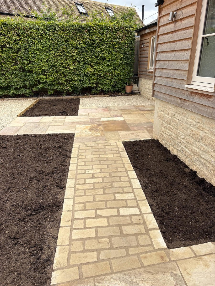 A sandstone path with freshly dug planting beds either side of a cottage