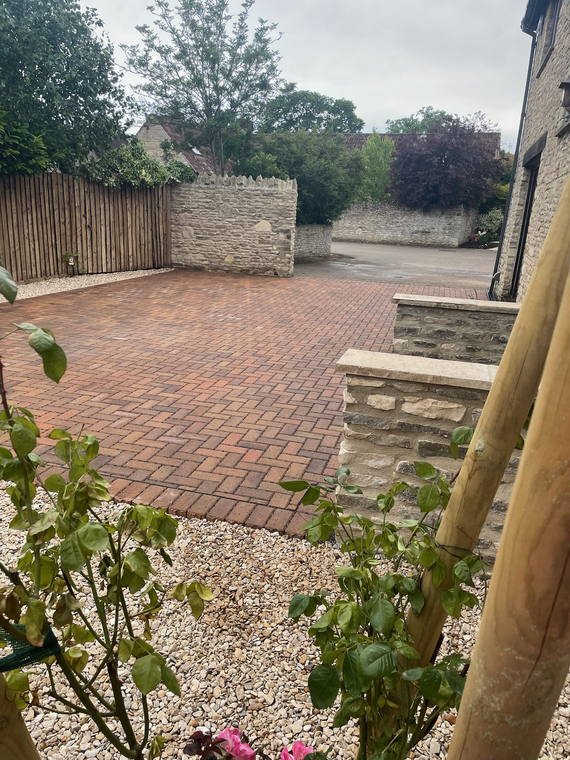 Block paving beside a new stone wall, with roses planted into a shingle bed