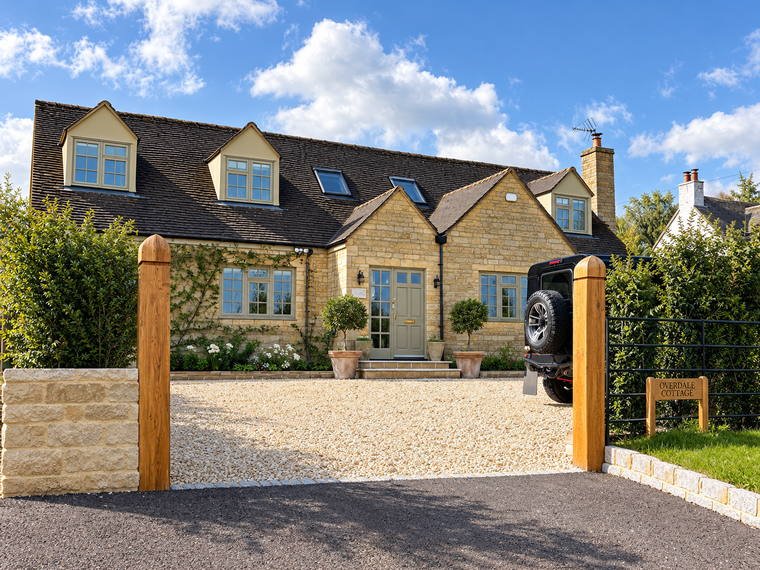 A Cotswold stone entrance with oak gate posts, granite cobble apron and a reshingled gravel drive