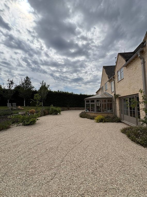 A gravel drive curving up to a Cotswold house under a heavy sky