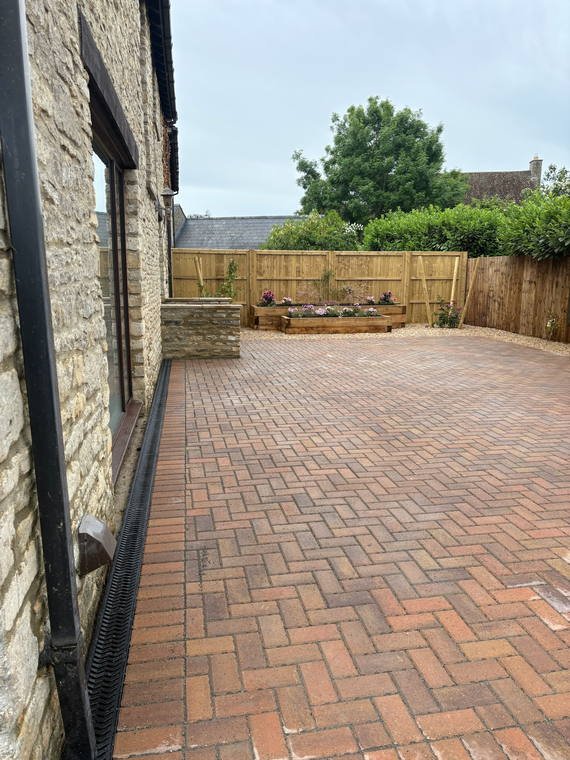 A herringbone brick courtyard wrapping the back of a Cotswold stone house