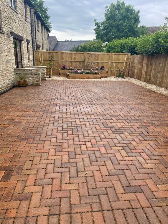 A driveway laid in herringbone block paving, running up to a stone house