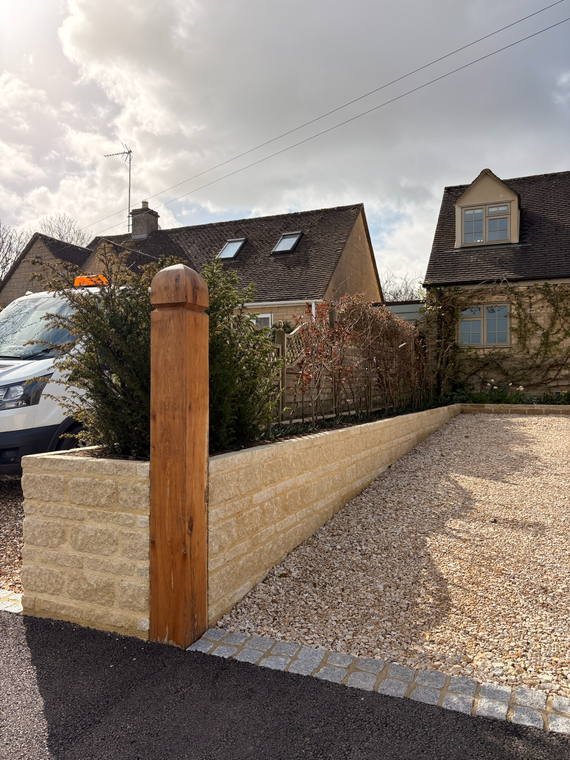 An oak gate post set into a new Cotswold stone wall beside a shingle drive