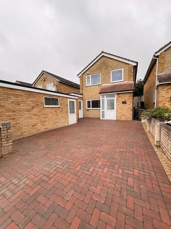 A red block-paved driveway running between two houses to the front door