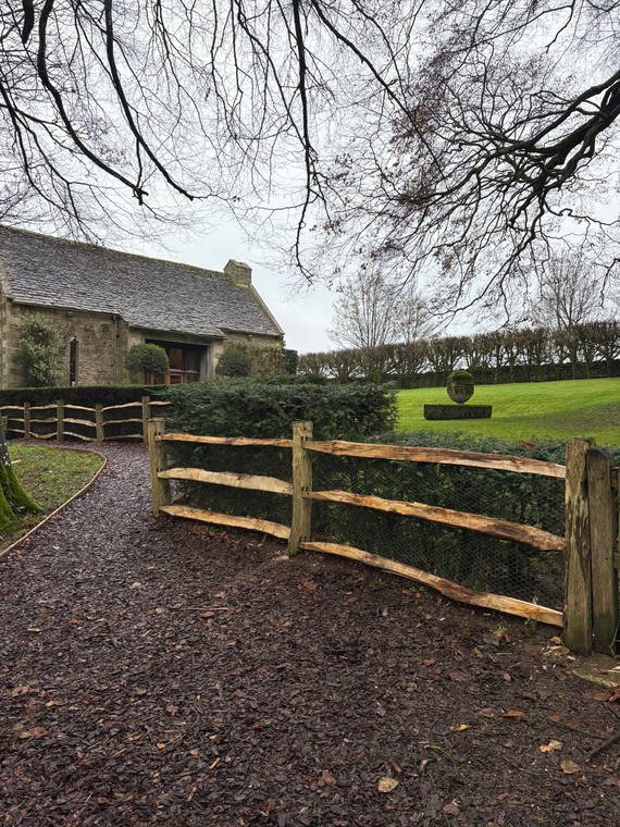 Cleft chestnut post-and-rail fencing running past a stone barn