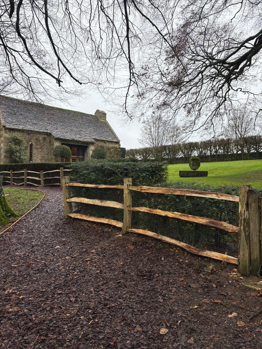 Cleft chestnut post-and-rail fencing running past a stone barn