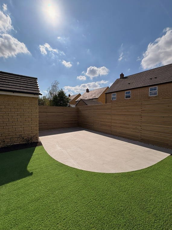 A curved resin patio meeting artificial turf, with a slatted timber screen behind
