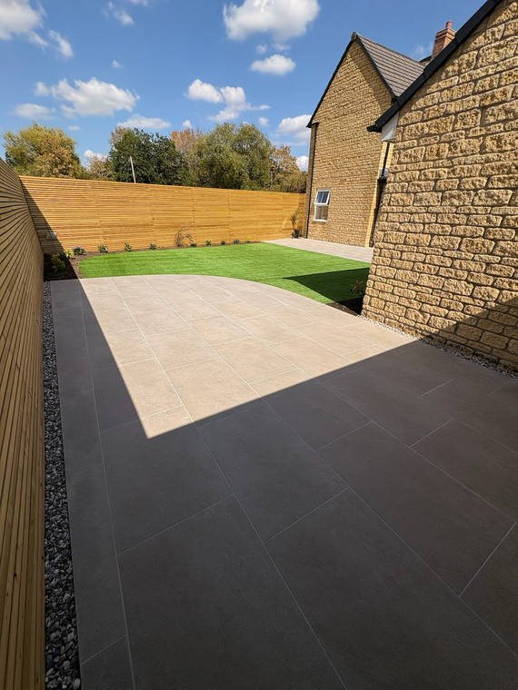 A dark porcelain drive and path beside a new lawn and timber fence