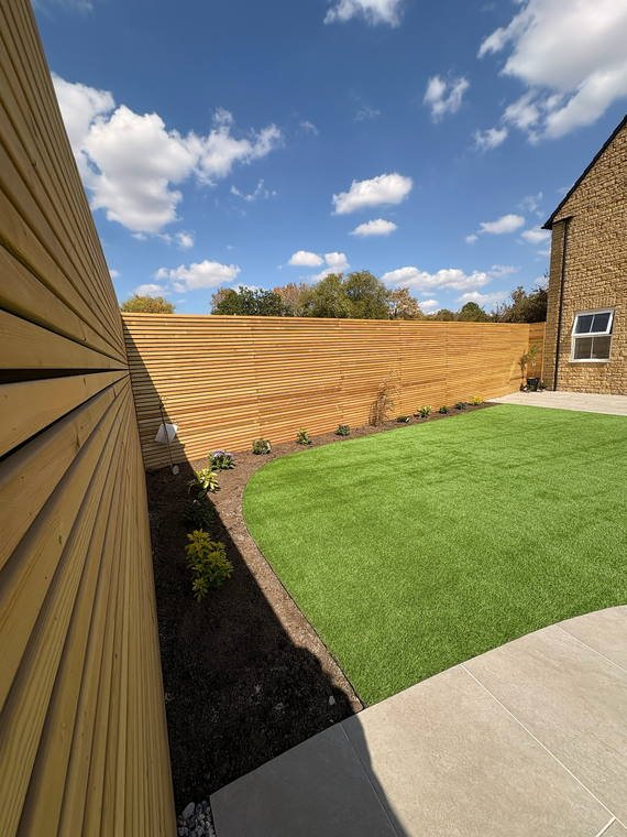 A slatted timber screen and close-board fence around a new lawn and porcelain path