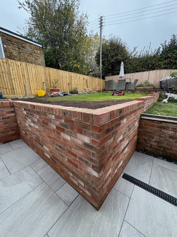 A brick retaining wall holding a raised lawn above a grey porcelain terrace