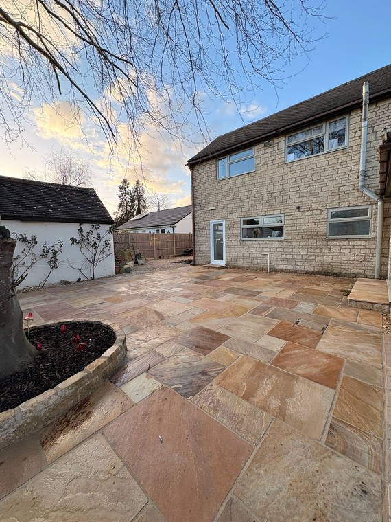 A sandstone patio with a curved stone-edged planting bed, late in the day
