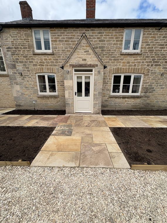 Sandstone paving and fresh planting beds across the front of a Cotswold house