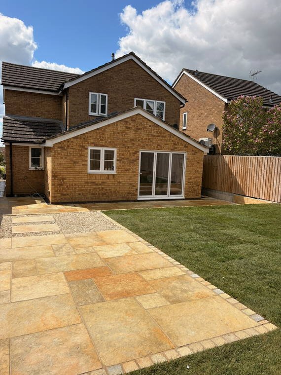 A sandstone patio meeting new turf behind a brick house