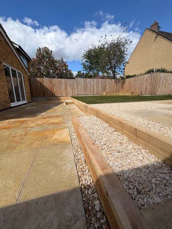 A sandstone patio with a sleeper edge and shingle margin against new turf