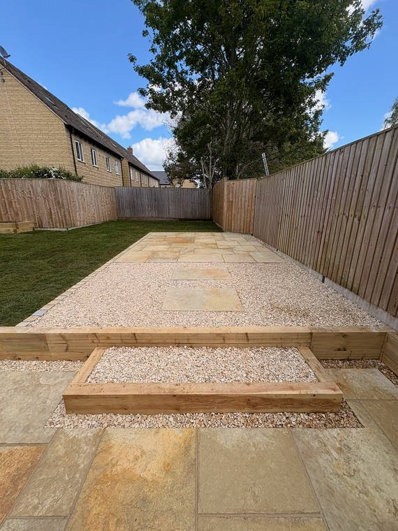 A sandstone path with a sleeper step up to a gravel area between fences