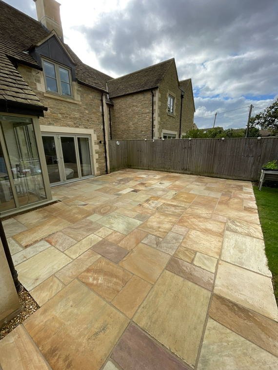 A broad Indian sandstone terrace laid across the back of a Cotswold stone house