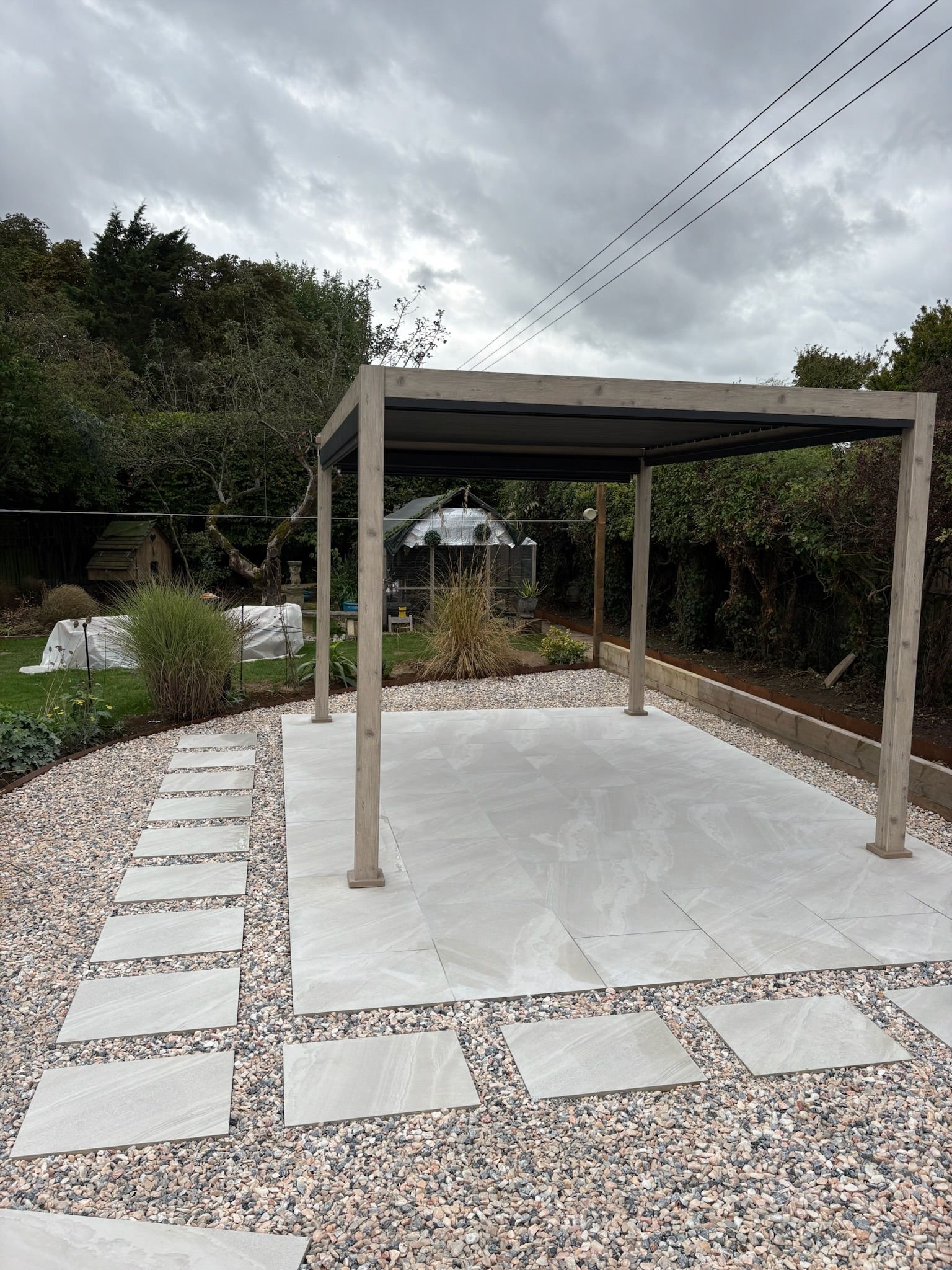 A pergola standing over a porcelain terrace with stepping stones through gravel
