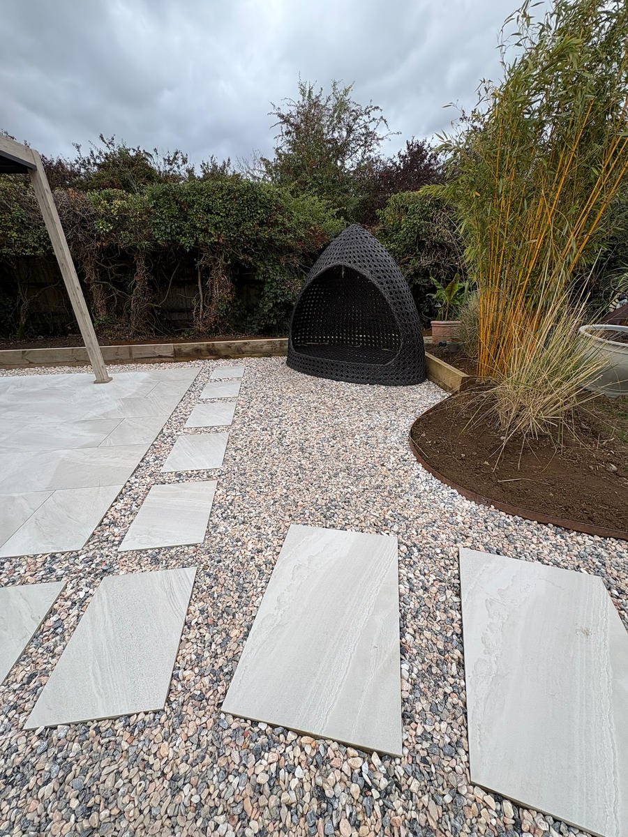 Large porcelain planks set through washed gravel, leading to a woven fire-pit dome