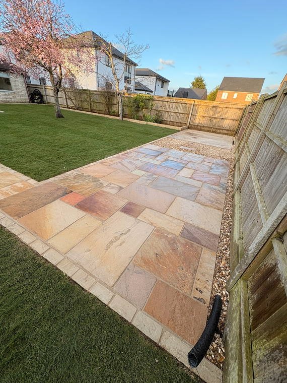 The edge of a sandstone patio meeting new turf and a shingle margin