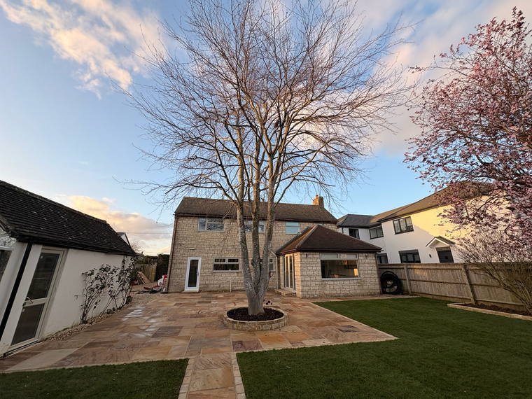 A wide Indian sandstone terrace wrapping a house with fresh turf and a tree in a stone ring