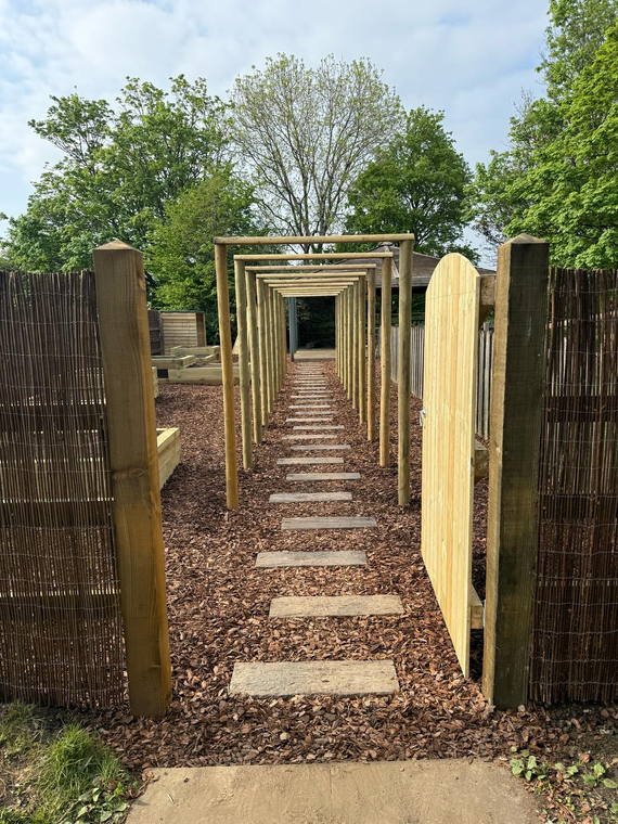 A timber archway walk with stepping stones and woven willow screening at a primary school