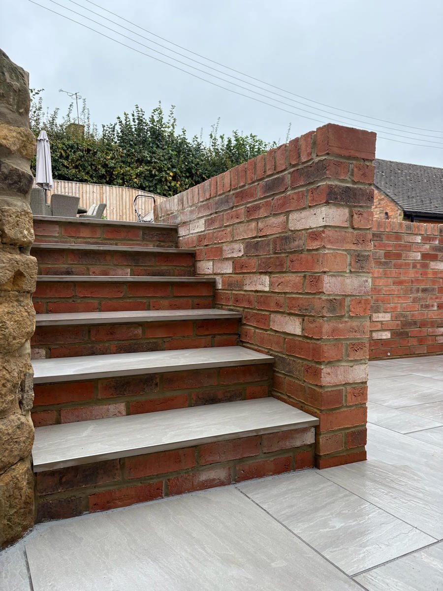 Brick steps with porcelain treads rising between a rockery and a brick retaining wall
