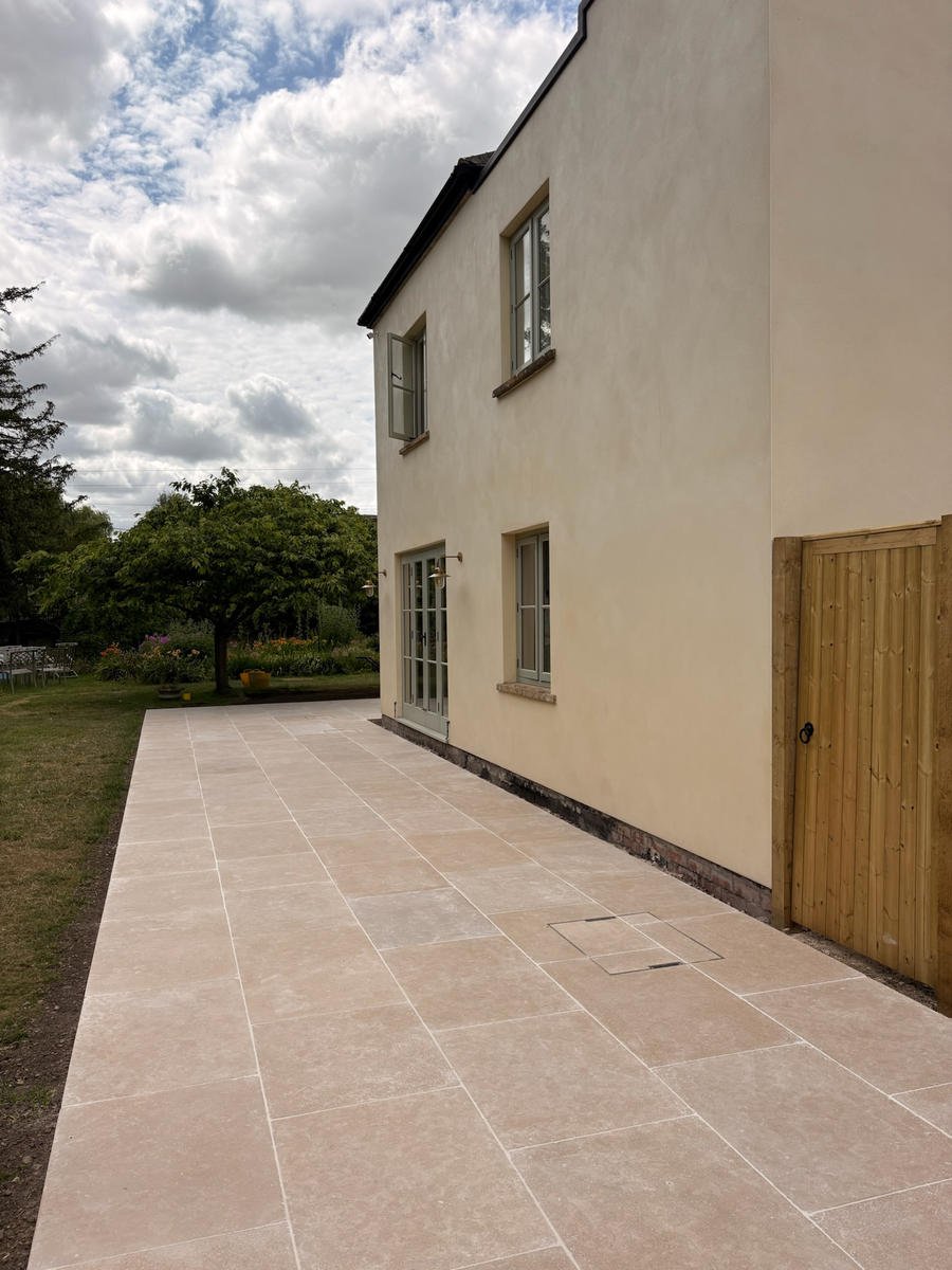 A large pale porcelain terrace running the length of a rendered house