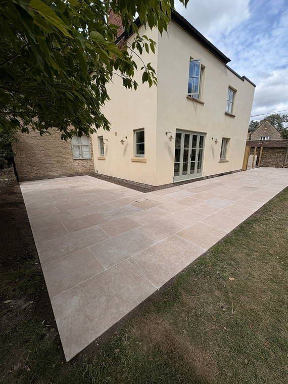 A porcelain terrace wrapping the corner of a rendered house onto new lawn