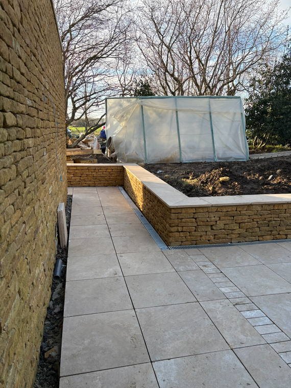 A stone-walled terrace holding a raised bed above new porcelain paving